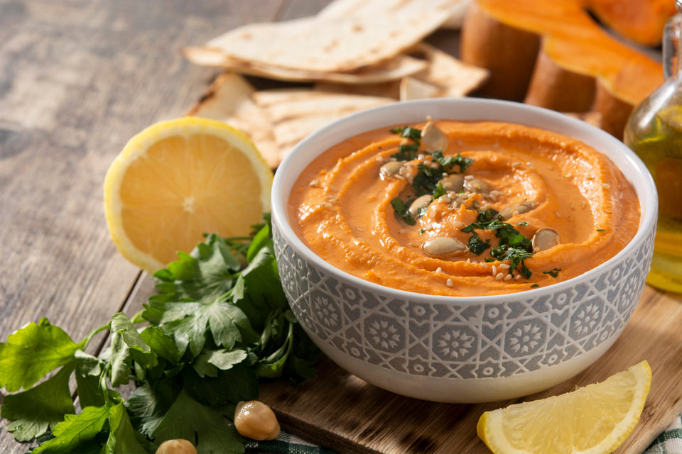 Bowl of Pumpkin Sage Hummus with herbs and lemon in the background